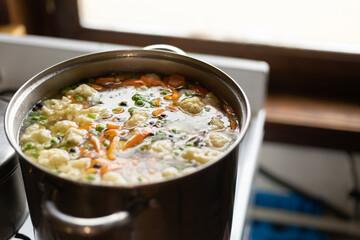 a pot of vegetable soup on the stove by the window