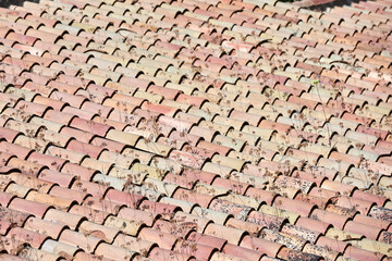 Old terracotta roof with rows of curved tiles in faded shades of red, pink, and beige, partially...