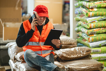 An older worker in a pet food warehouse prepares deliveries of goods for pet stores.