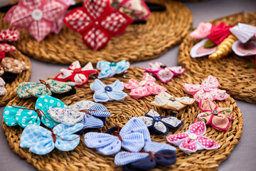 Colorful handmade fabric butterflies and bows arranged on woven straw mats, featuring patterns,...