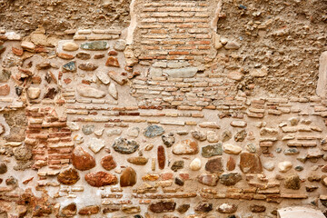 Old wall made of mixed stone and brick with visible mortar lines, earthy tones, and uneven surface,...
