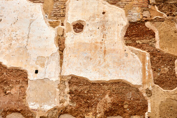 Old wall with exposed bricks, rough surface, and faded plaster in earthy tones, showing signs of...