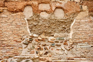 Aged wall with visible bricks, scattered stones, and patches of worn plaster in earthy tones,...