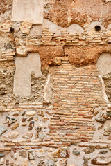 Old wall with exposed red bricks, natural stones, and patches of worn plaster in earthy tones,...