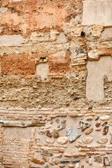 Old wall with exposed bricks, embedded stones, and patches of worn plaster in earthy tones, showing...