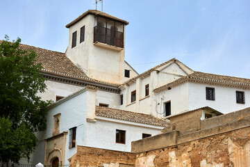 Fototapeta premium Whitewashed Mediterranean building with tiled roofs, small windows, and square tower against blue sky, showing traditional architecture and structure; architecture, facade;