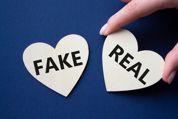 Real or Fake symbol. Concept word Real or Fake on wooden hearts. Beautiful deep blue background....