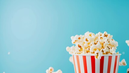 Popcorn exploding from a striped bucket on a blue background. Movie night and entertainment concept. Footage for a cinema advertisement, film festival promotion or a snack food commercial
