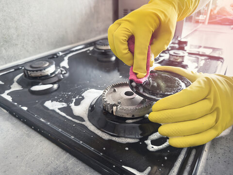 Hands cleaning gas cooker with special white foam in the kitchen