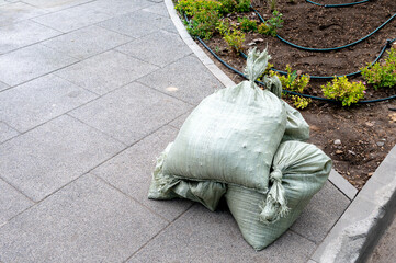 Green bags with soil or landscaping materials on the pavement next to a flowerbed in a new public...