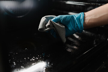 Close-up hands of unrecognizable man in blue gloves cleaning inside of oven with gray rag, ensuring...