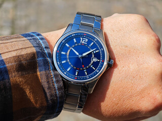 Man Wearing Elegant Wristwatch Outdoors. Man’s wrist wearing a sophisticated analog watch with a blue dial and silver case