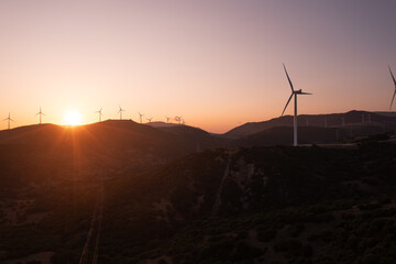 Wind turbines stand silhouetted against a breathtaking sunset, generating clean energy amidst...
