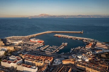 An aerial view of Tarifa's bustling port, featuring a large ferry docked, numerous boats in the...