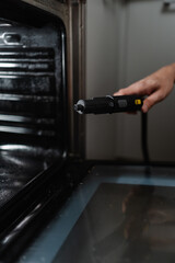 Close-up vertical shot of man sanitizing gas oven using steam cleaner, working to eliminate grime...