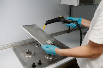Housewife male wearing protective gloves sanitizing kitchen extractor filter using high-pressure...