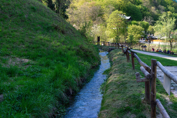 Narrow forest trail running alongside a small stream, bordered by a rustic wooden fence in a lush green spring landscape in Ojc&oacute;w, Poland.