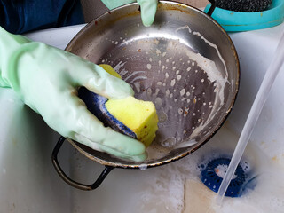 Housewife washing a dirty stainless pan, washing greasy dishes with detergent under water in the sink.