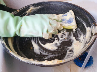 Female housewife washes a dirty non-stick skillet after a meal in the sink. Washing greasy, dirty dishes under water in the kitchen.