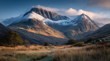 Scenic view of Glen Coe, Scotland, on a sunny day with light snow dusting the peaks of the steep mountains and a field of tall golden grass