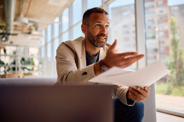 Male entrepreneur talking while analyzing business reports in the office.