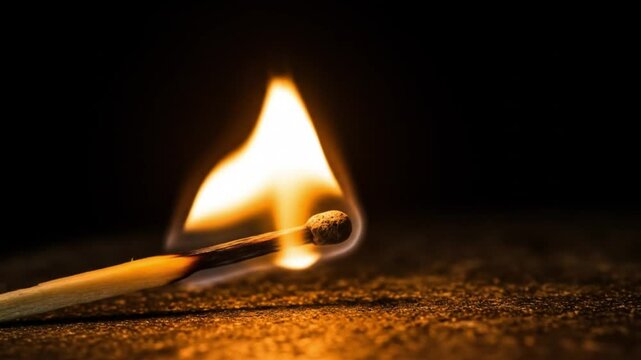 Burning matchstick with flame against dark background  