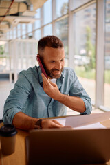 Happy entrepreneur talking on the phone while going through business reports in the office.