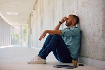 Tired businessman holding his head in pain while sitting on the floor in the office.