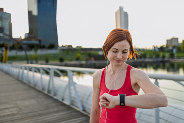 Runner checking her performance on a smartwatch during her morning run across a city bridge.