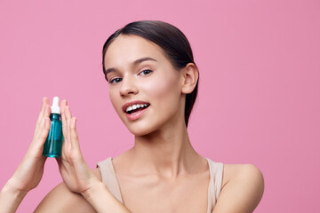 Young woman holding a beauty serum on a pink background, showcasing clear skin and a glowing smile,...