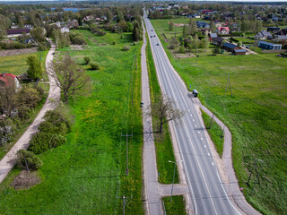 An aerial view of a straight two lane road bordered by open fields, scattered houses, trees,...