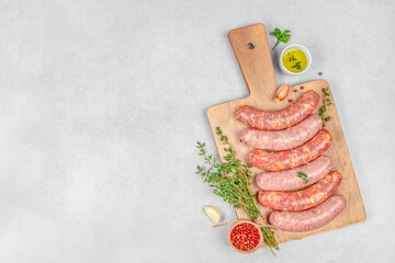 A rustic arrangement of raw sausages with herbs, oil, and spices on a wooden cutting board over a...
