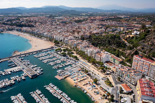 An aerial view of Blanes showcasing a beautiful bay with clear turquoise water, rocky cliffs, and numerous white villas nestled among green trees on the hillsides