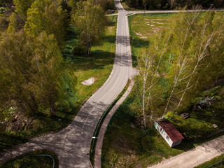 An aerial view shows intersecting roads, open grassy areas, sparse trees, and a small red roofed structure with white walls in the lower right corner.