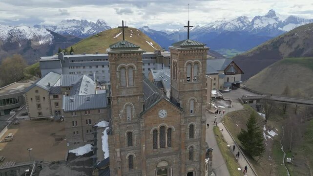 Close-up of the Basilica of Our Lady of La Salette in the French Alps, surrounded by lush forests and snowy mountains. Site of the 1846 Marian apparitions.