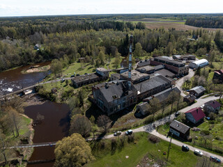 An industrial complex with a tall smokestack, large buildings, a river with a dam and pedestrian...
