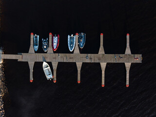 Aerial perspective of a wooden dock with red tipped edges, six moored boats in various colors, and...