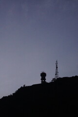 Silhouette of a mountain and communication tower against a cloudy sky at dusk