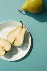 White plate with green pear half fruit on the blue background