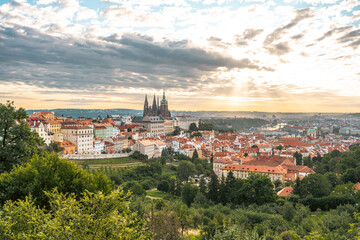 Fototapeta premium At sunrise, a stunning view of Prague Castle emerges amidst a picturesque landscape. The early light casts golden hues over the city's rooftops and greenery, creating a serene atmosphere.