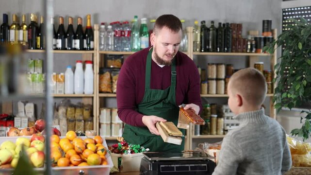 Friendly middle-aged salesman offering turrons to little boy in grocery store. High quality 4k footage