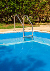Metal pool ladder leading into calm turquoise water. Clean and minimal summer scene perfect for...