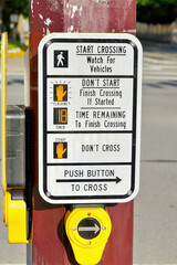 Pedestrian crossing sign with detailed instructions at a sunny street intersection.