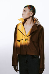 Young woman with colorful stylish short hair wearing brown leather jacket and denim, posing against...