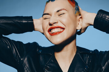 Young woman with colorful short hair smiling broadly, wearing black leather jacket against clear...