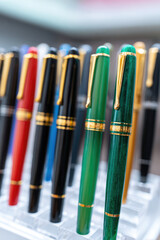 Fountain pens with gold accents are displayed upright in a rack. Writing instruments variety and color