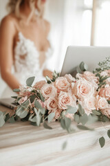 A woman in a bridal dress is near a laptop surrounded by pink roses on a wooden table. Concept: wedding planning, romance, elegance