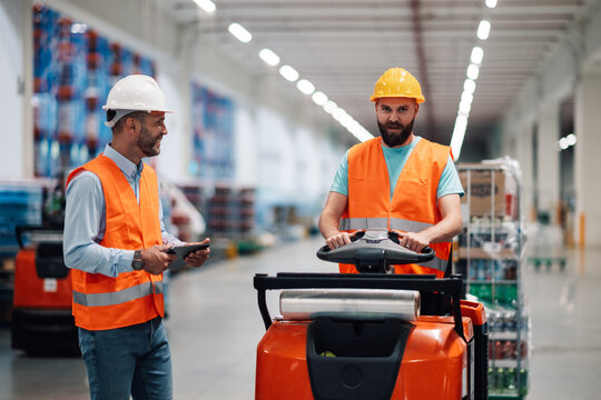 Warehouse workers managing inventory with forklift and digital tablet