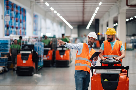Warehouse manager guiding worker driving forklift with digital tablet