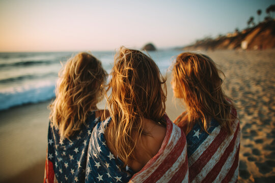 Three women at the beach wearing U.S. flags. Celebration and patriotism. National holiday, summer fun, freedom. Independence Day. Fourth of July.